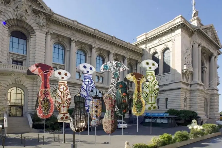 Five giant sculptures of brightly painted body-shaped figures outside an ornate sandstone building.