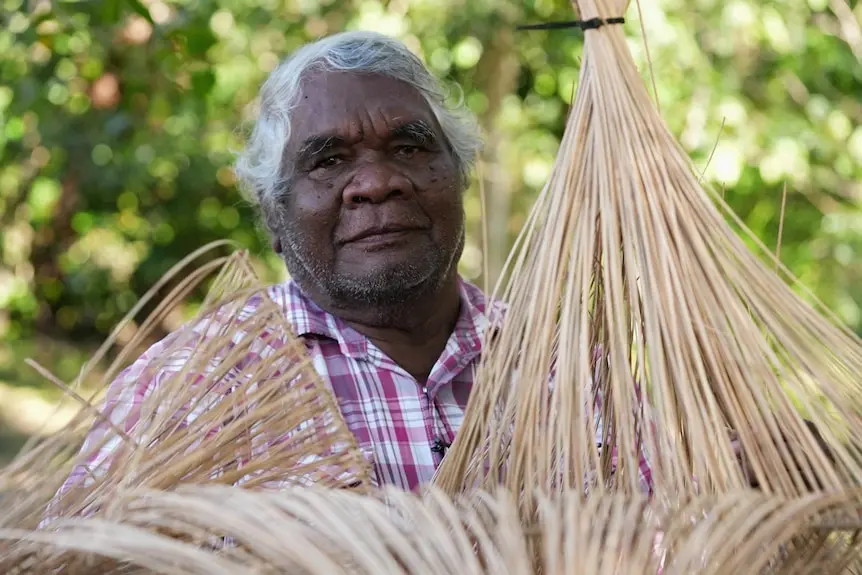 An elderly Aboriginal man sits with baskets made from lawyer cane.