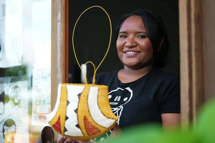 A young Indigenous woman smiles while holding a colourful basket.