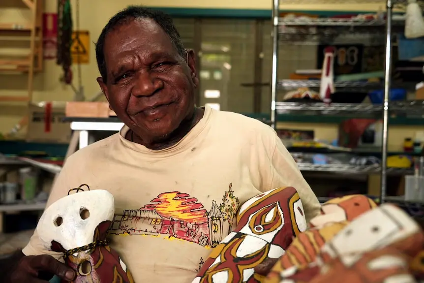 An elderly AboriMan paints a ceramic figure in an art workshop.