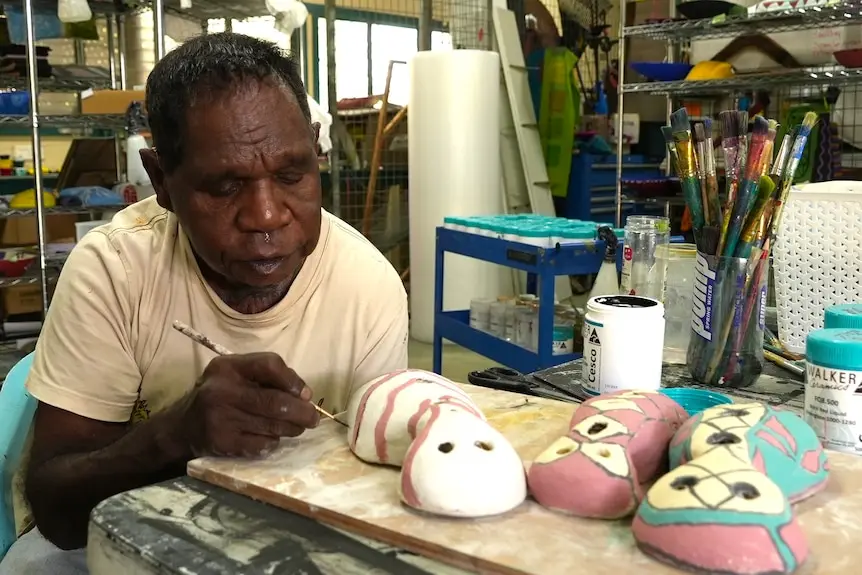 An Indigenous man carefully paints a clay sculpture in an art workshop.