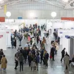 Groups of people walking through the aisles of an art fair.