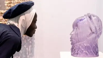 A Black woman gazes at a lilac-colored glass sculpture. 