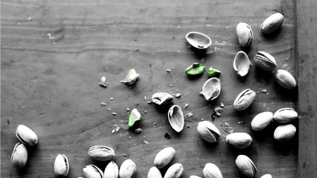 Fresh pistachios and their broken shells on a flat woody surface