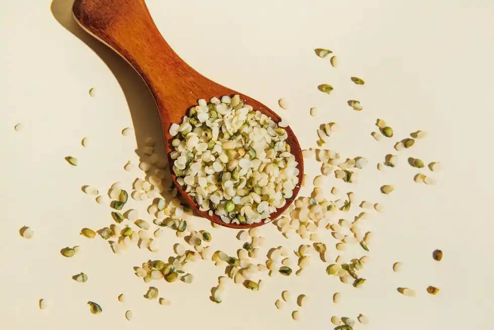 wooden spoon with purified and ground hemp seeds on beige background hemp food supplements flat lay, top view