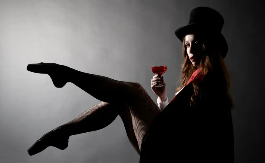 City Ballet of San Diego dancer Ariana Gonzalez is shown as Dracula in an undated photo. She is wearing pointe shoes, but her feet are in silhouette. She's holding a stemmed glass full of red liquid, and a top hat. Her eyes and lips are bright red. 