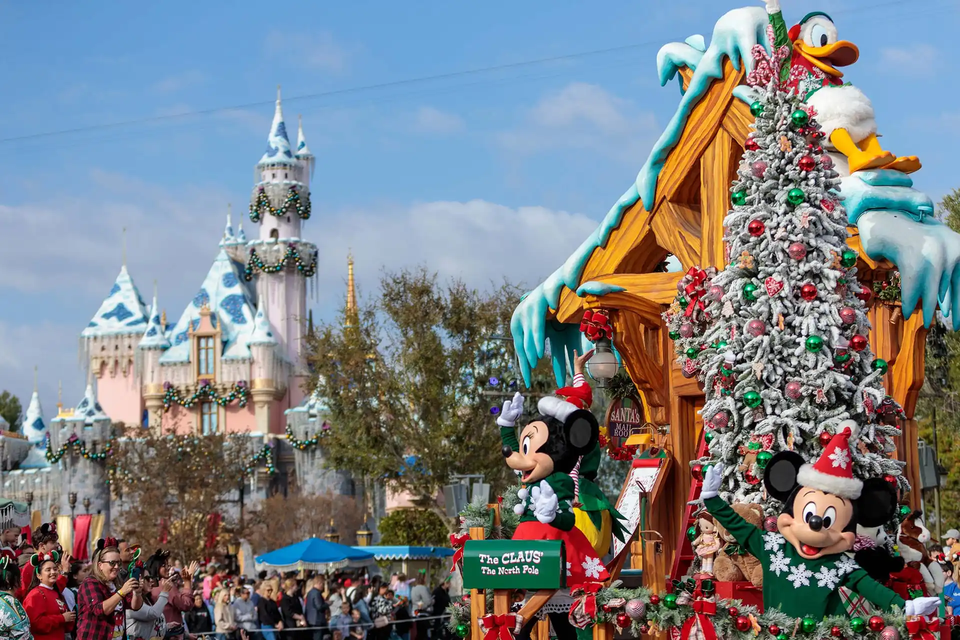 A Disneyland parade with a holiday-themed float featuring beloved cartoon characters and a festively decorated tree, set against the enchanting backdrop of a castle and an excited crowd.