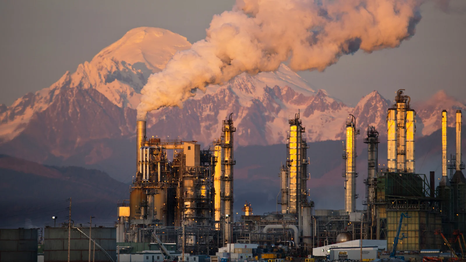 A photo of an oil refinery at sunset with a mountain in the background