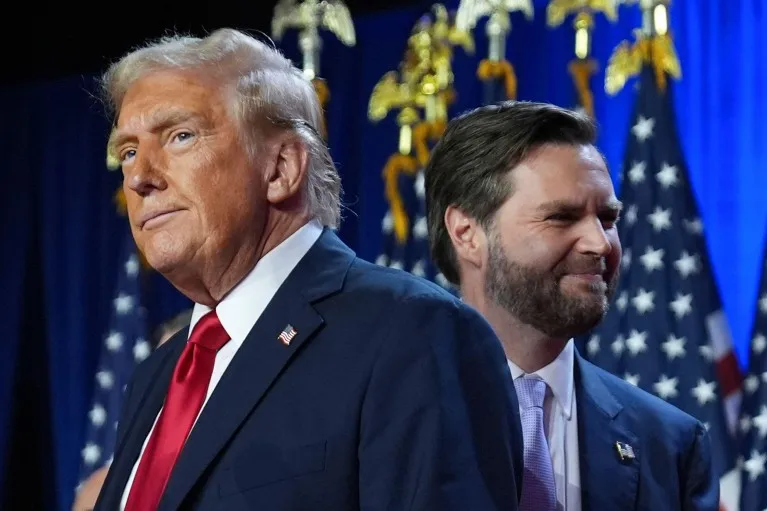 Donald Trump and J. D. Vance standing on a stage in front of American flags