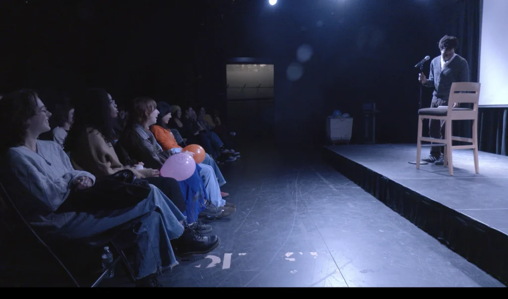 Elijah Groves performs standup comedy on stage with audience members looking on