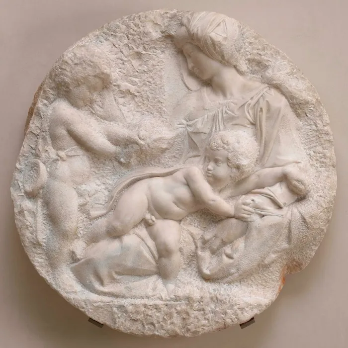 A  white marble circle carved with depictions of Mary with the baby Jesus and another saint as an infant