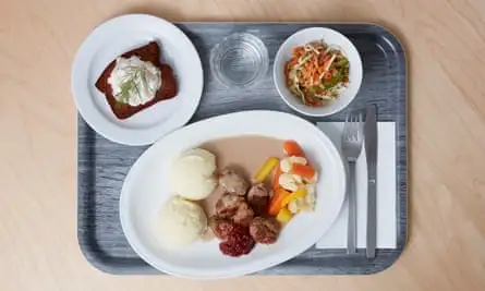 A grey plastic tray with cutlery and a napkin a plate of meatballs in a sauce, mashed potato and vegetables, with a bowl of salad, a glass of water and a piece of toast with a topping