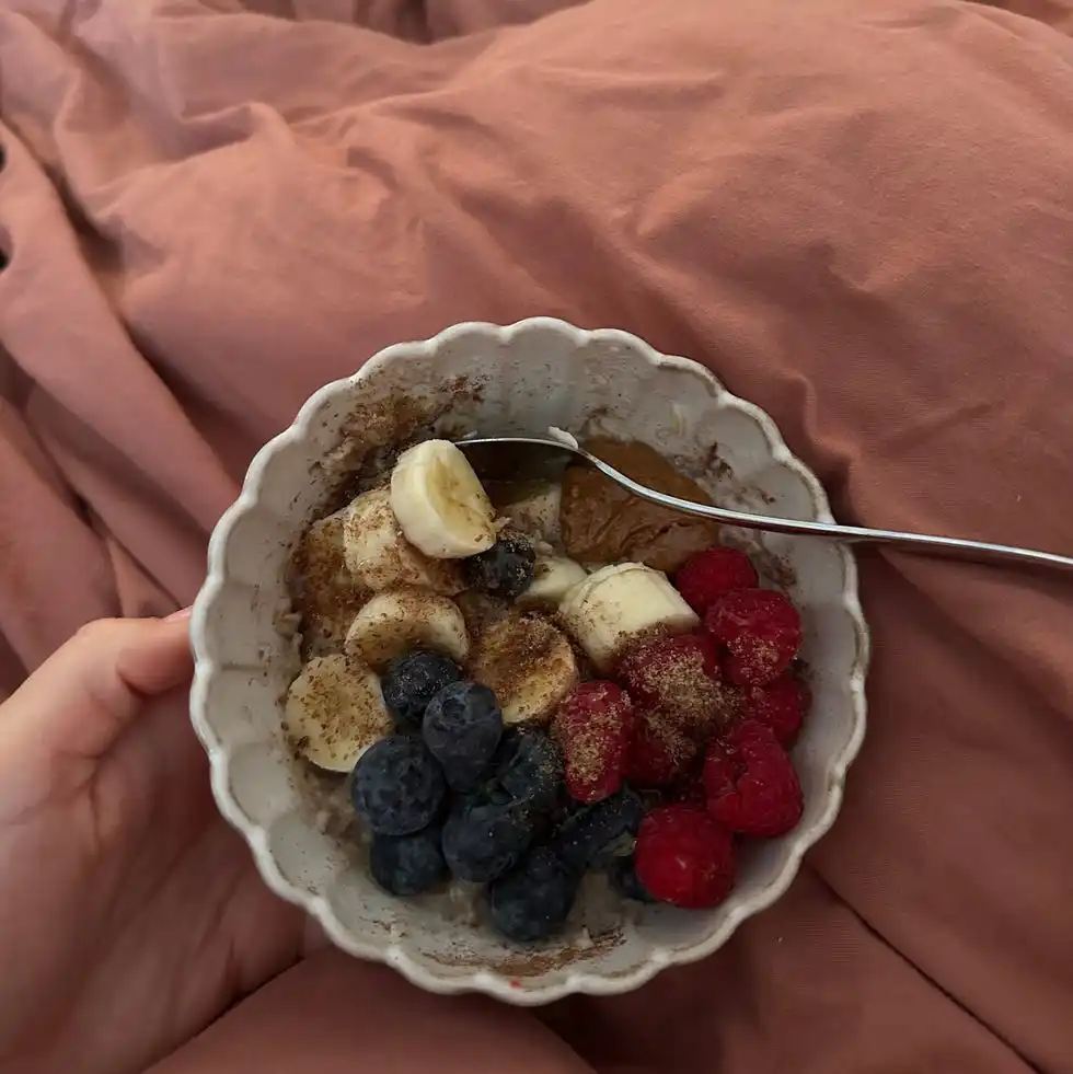 bowl of oatmeal topped with fruits set against a bed with pink bedding