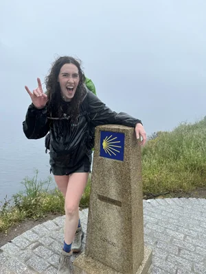 A student poses for a photo while standing by a marker for a hiking trail.