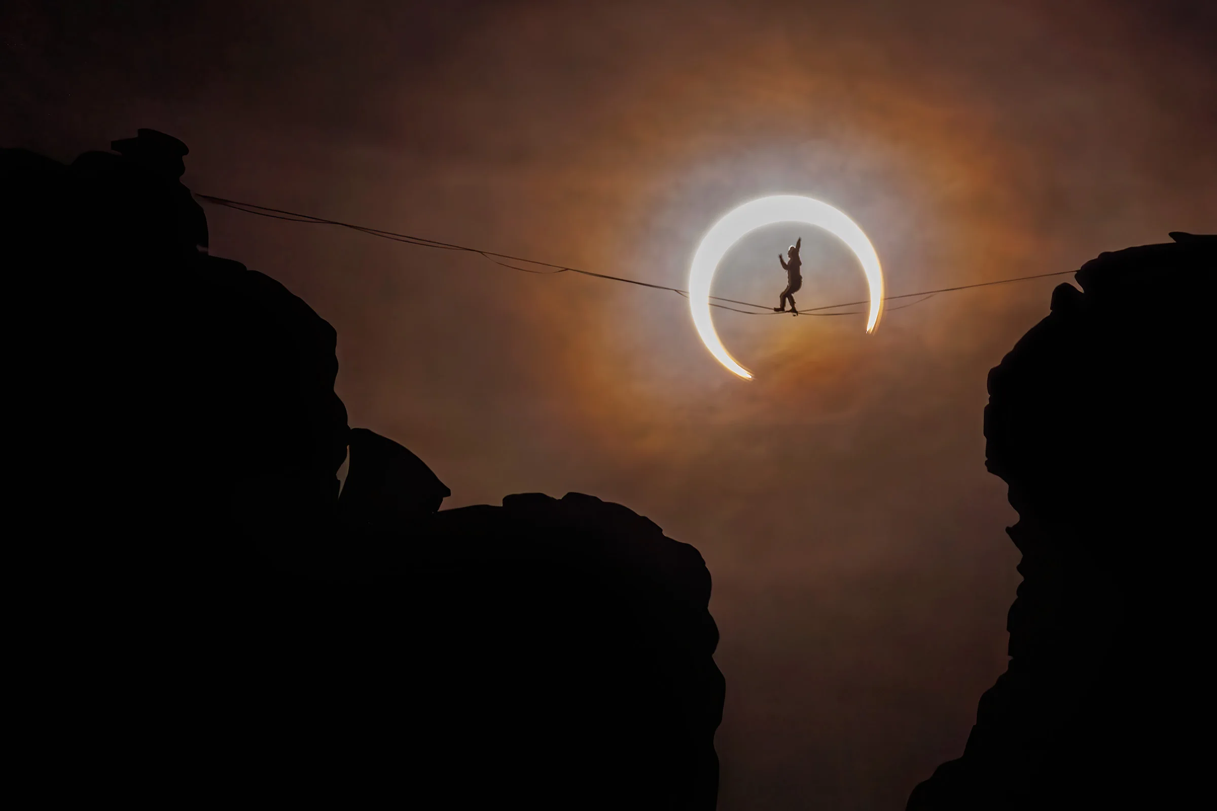 a person on a tightrope walks in front of the solar eclipse. a crescent of the sun shows