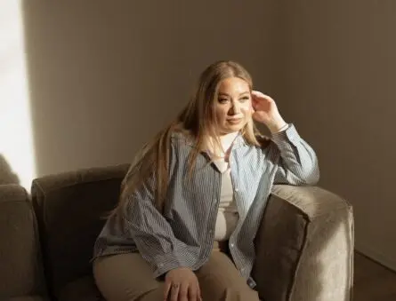 A woman sits on a couch with dramatic lighting.