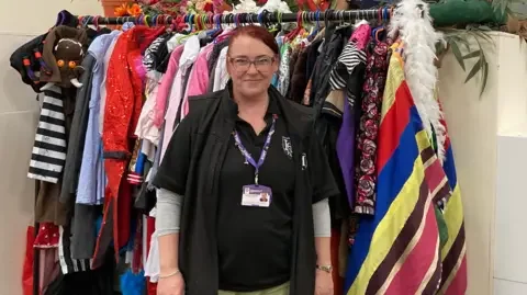 BBC Eleanor 'Elle' Dicks, founder of Haddon Charity of Performing Arts, standing in front of a multi-coloured costume rack. 