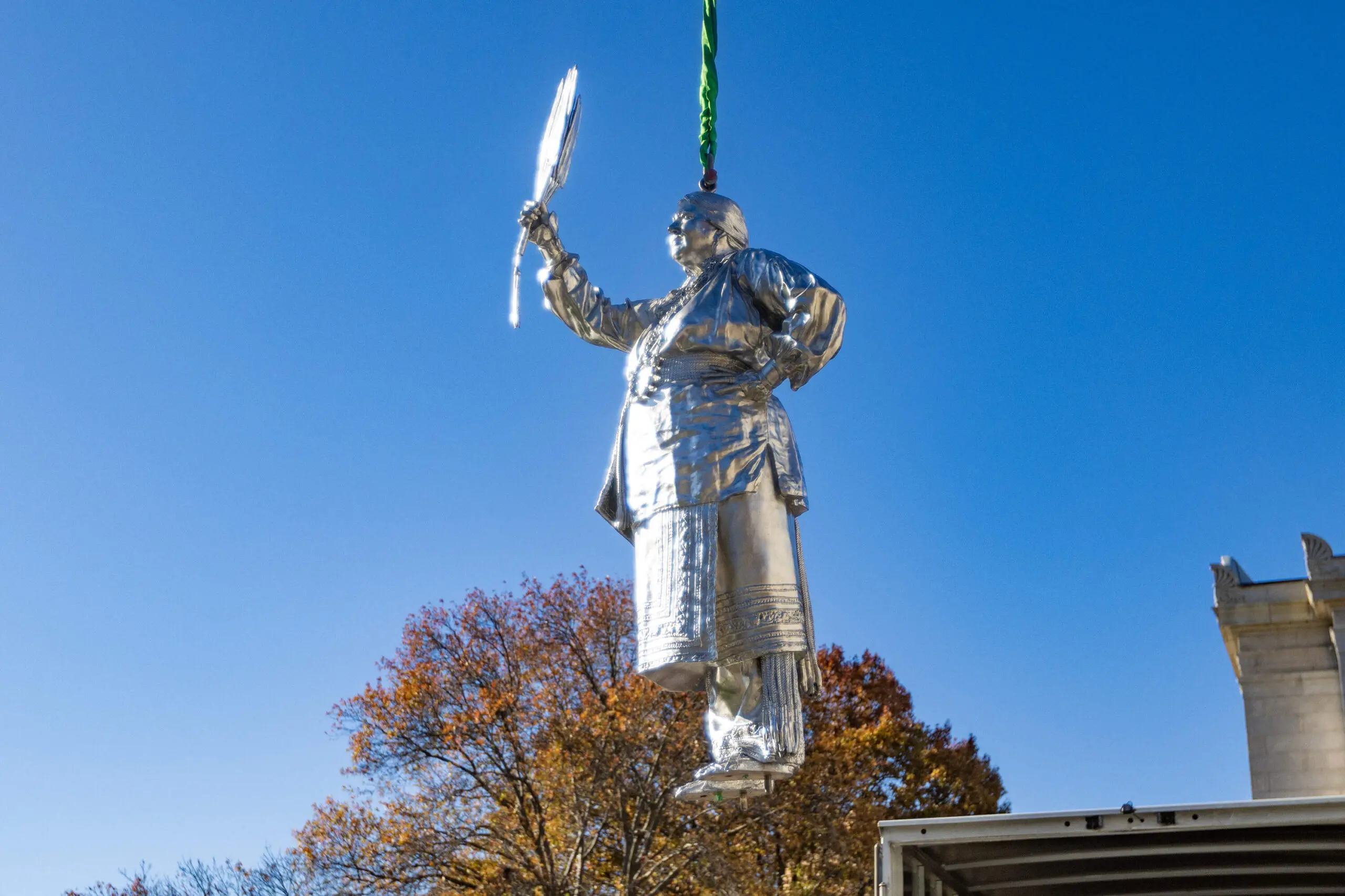 The statue of Aquinnah Wampanoag member and artist Julia Marden is raised by a crane out of its crate to be placed onto one of the two large plinths outside the Museum of Fine Arts main entrance, part of The Knowledge Keepers by Alan Michelson. (Jesse Costa/WBUR)