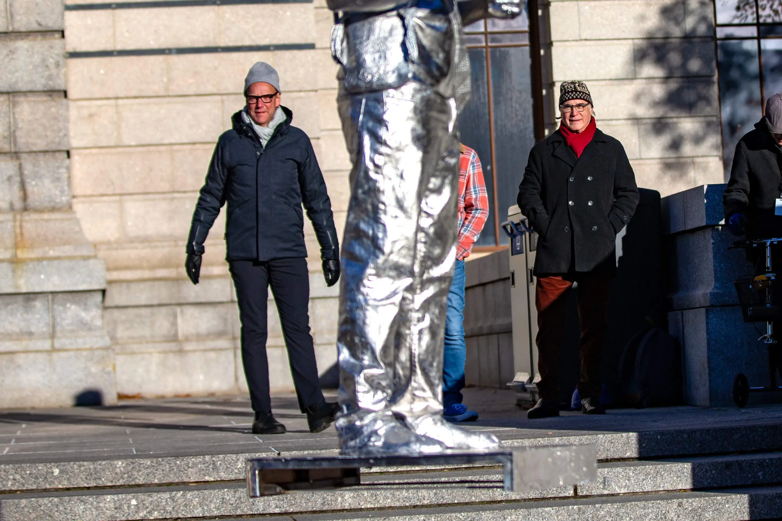 Ian Alteveer, chair of the department of contemporary art, left, and artist Alan Michelson watch as the statue of Nipmuc descendant Andre StrongBearHeart Gaines, Jr is raised to be placed on one of the large plinths outside the Museum of Fine Arts main entrance on Huntington Avenue. (Jesse Costa/WBUR)