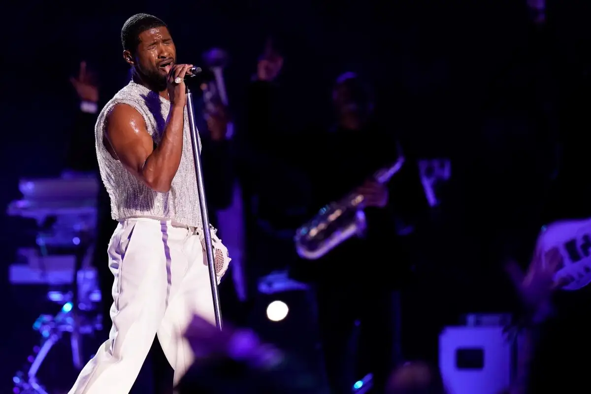 Usher, dressed in white, sings into a microphone onstage