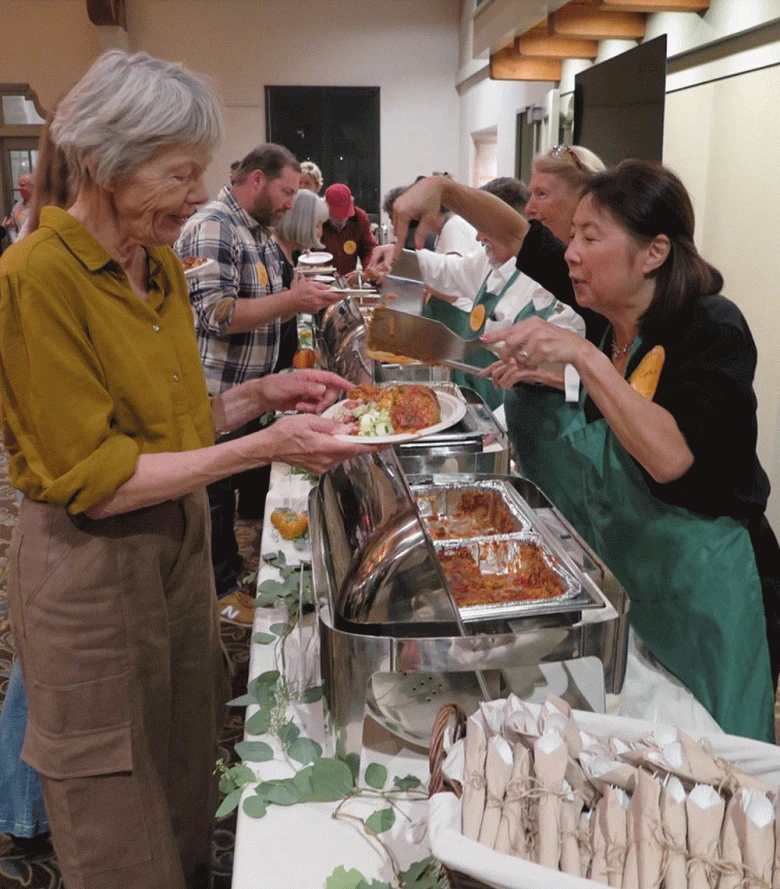 Servers wearing green aprons spoon food onto plates of attendees at Organic Soup Kitchen's anniversary event. (Courtesy photo)