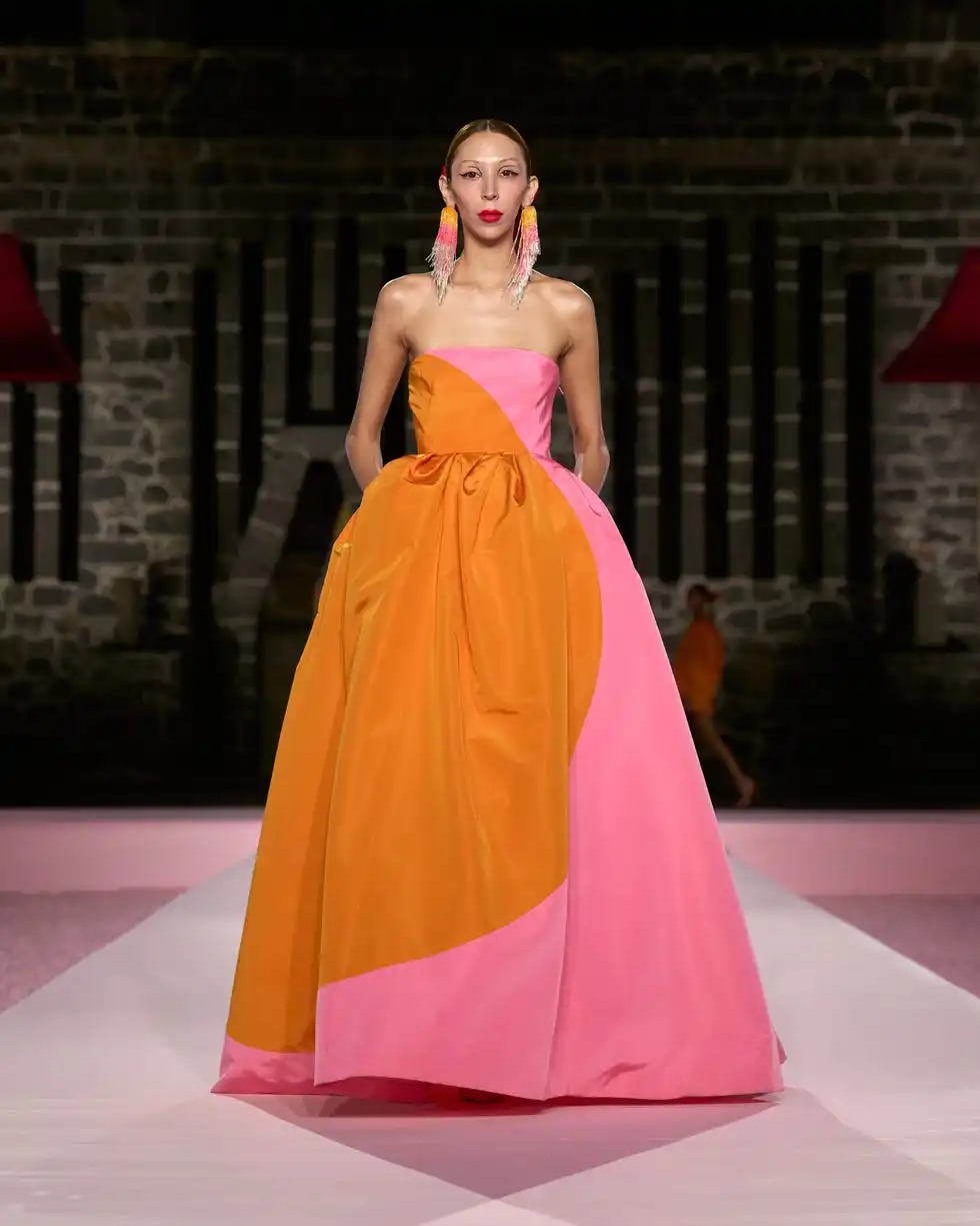 a model showcasing a vibrant pink and orange colorblocked gown on a runway