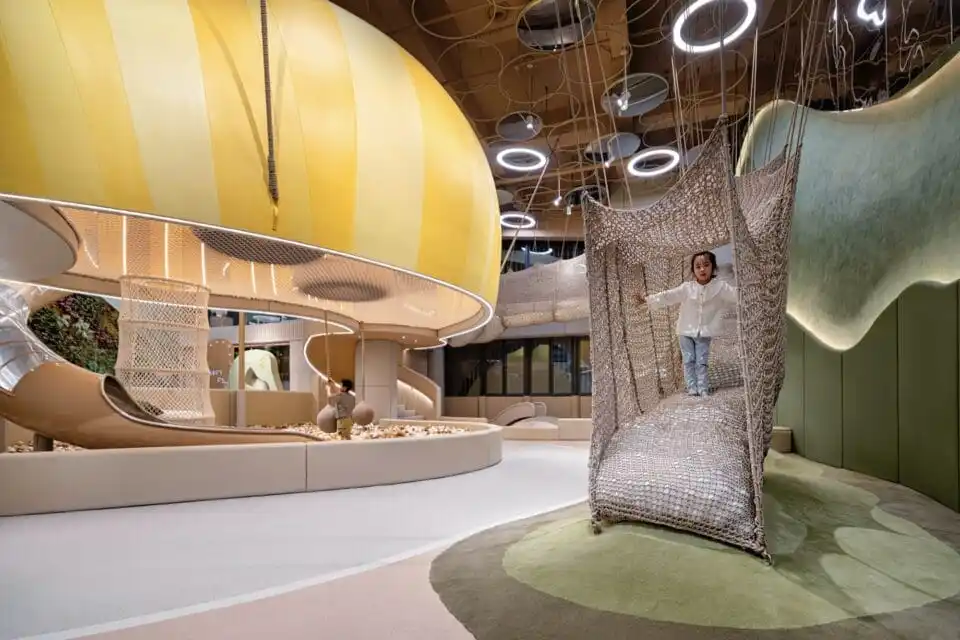 a child walks down a soft, netted form in a play area with giant mushrooms and other natural details