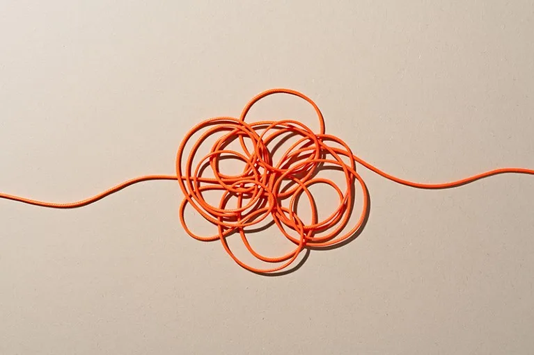 Orange coloured ropes tangled in a knot on beige background