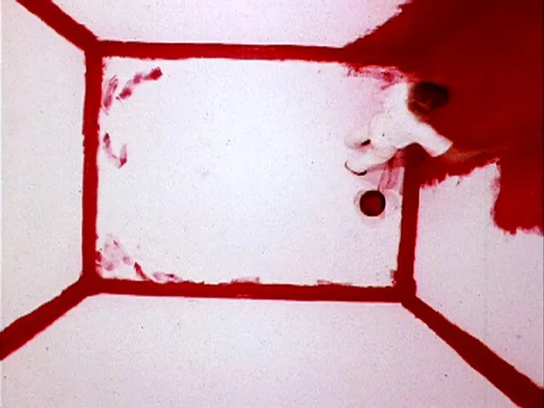 Overnight photo of an artist dressed all in white, in a white room, which they are painting red. One corner is red as are the corners of the room.