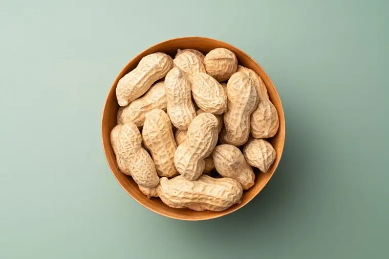 Whole Peanuts in Wooden Bowl on Green Background