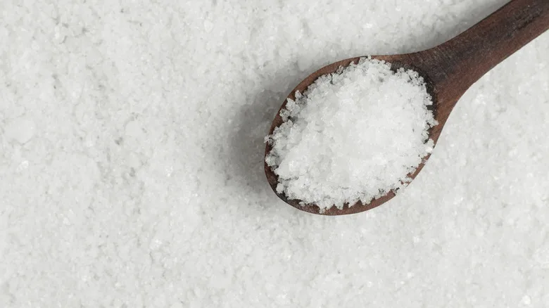 Wooden spoon with salt on a salt background