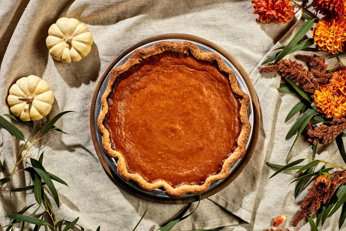 Pumpkin pie in an overhead photo, two mini albino pumpkins next to it