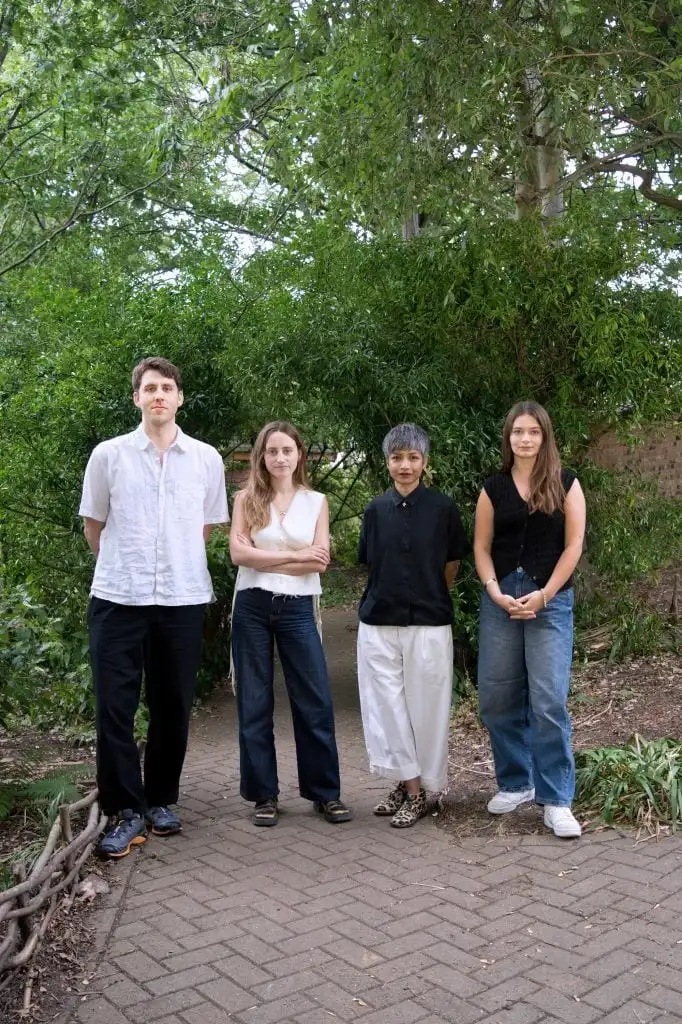 4 people stand in a row outside near trees