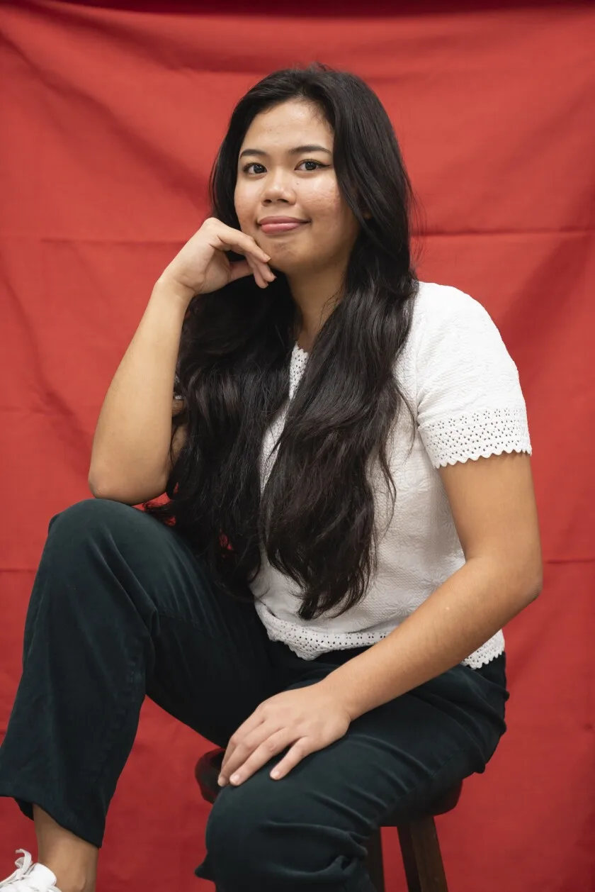 A woman poses on a chair against a red background.