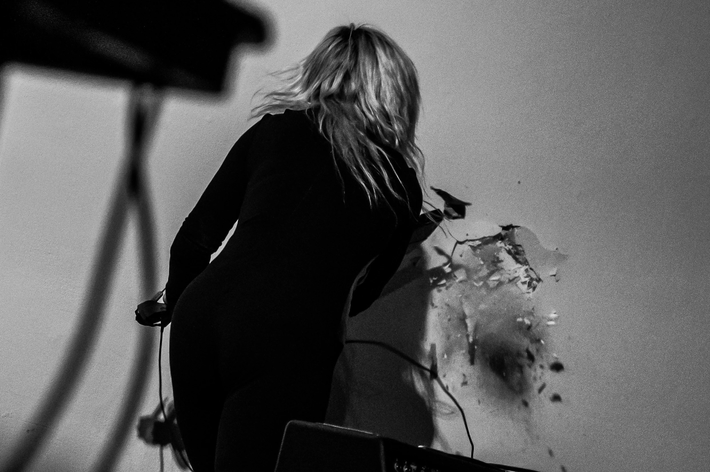 Person in black clothing facing a wall, using a tool to chip away at the plaster.