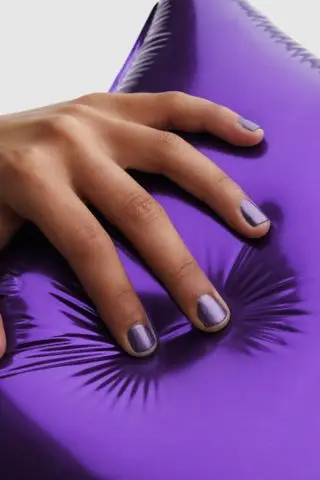 A hand holding a purple balloon wearing Pleasing x JW Anderson purple nail polish