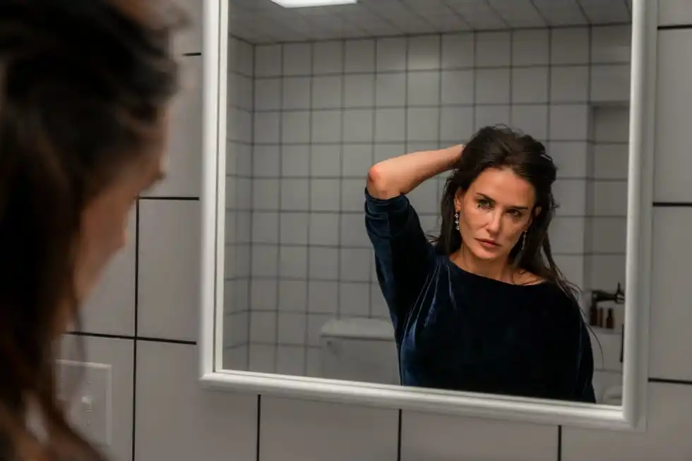 A person looking in a bathroom mirror adjusting their hair