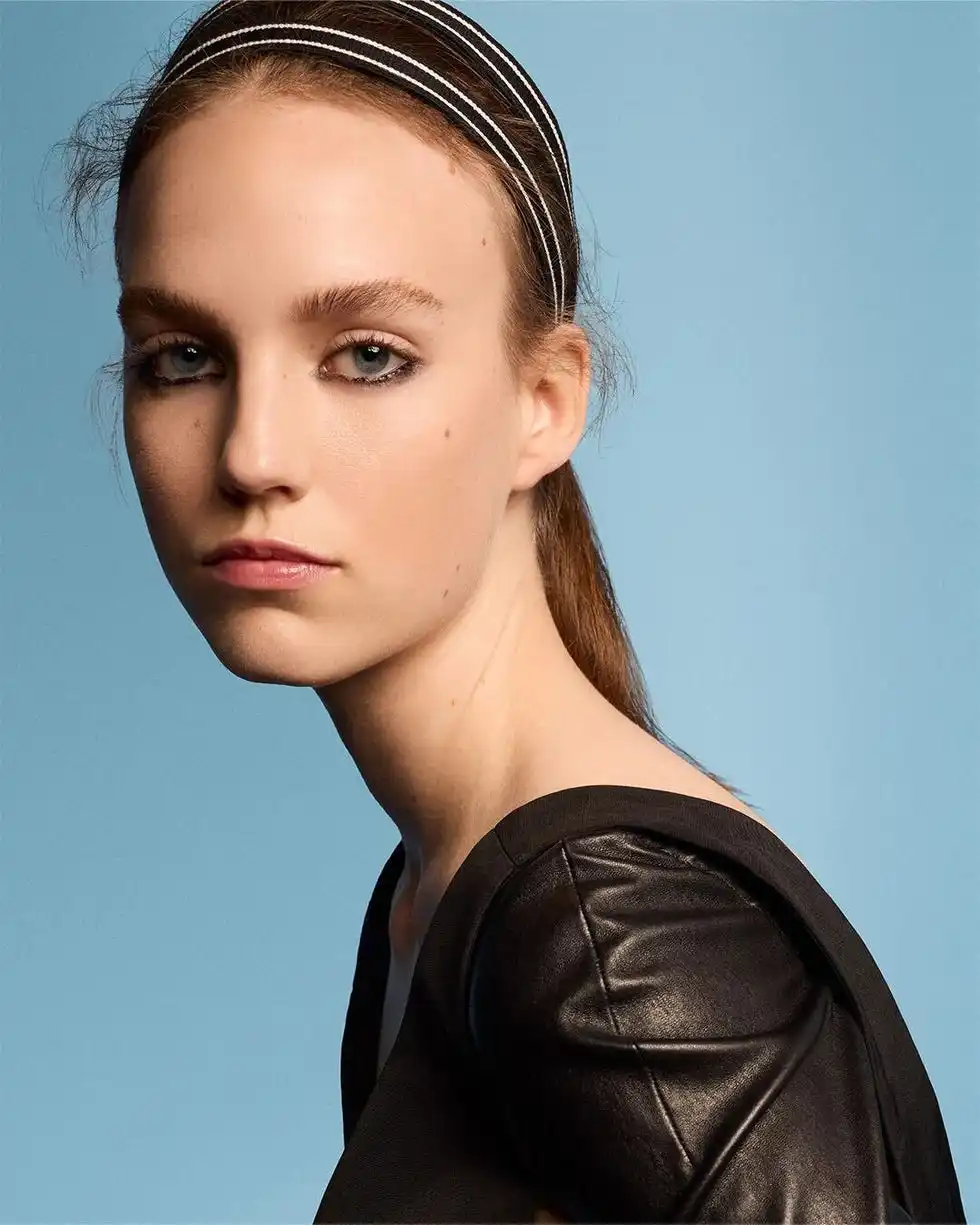 profile of a person wearing a stylish black outfit with a headband against a blue background