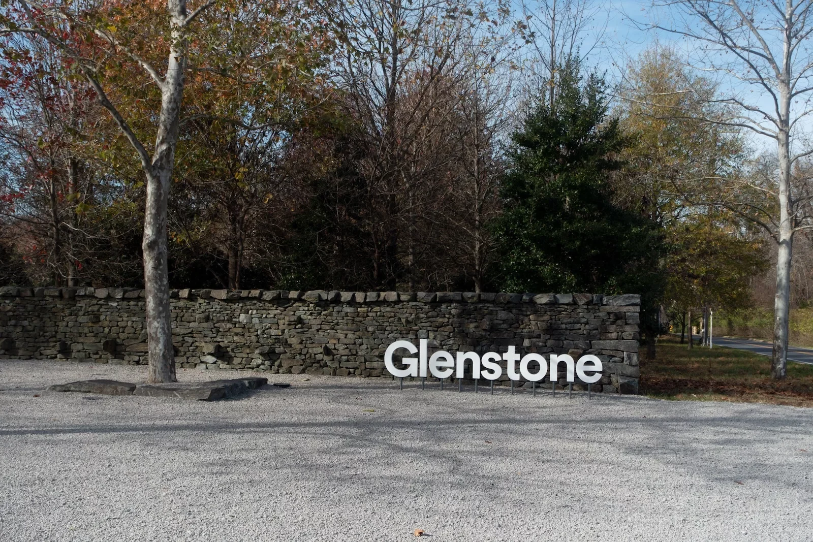 A photo shows a low stone wall with a name in front of it, “Glenstone” in white, each letter anchored to the ground under it. A tree stands tall in the left foreground.