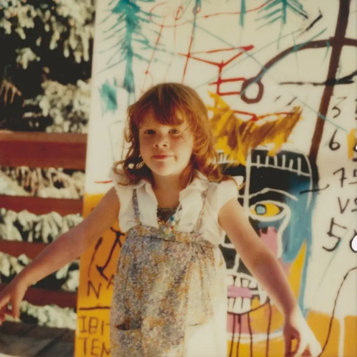 A young girl stands in front of a large Basquiat canvas 