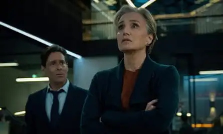 Diana Taverner, played by Kristin Scott-Thomas, looks alarmed as she looks towards a screen, with Claude (James Callis), looking at her from behind her right shoulder.