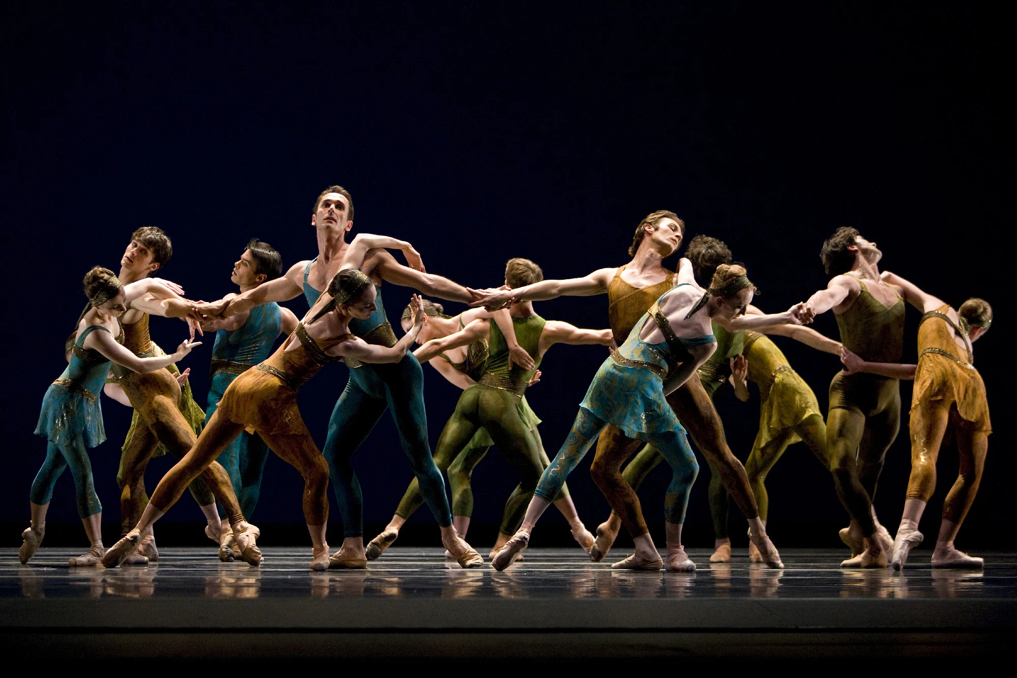 line of dancers in jewel tones entwined against black backdrop