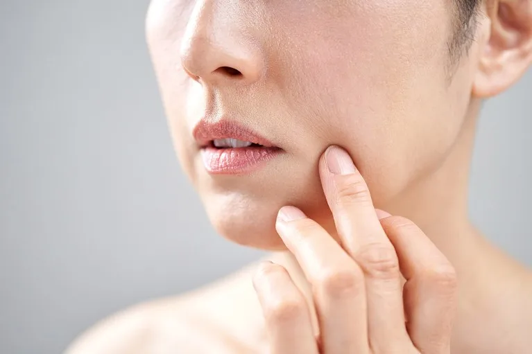 Close up view of a middle-aged Japanese woman touching the skin on her cheek.