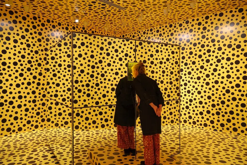 Bright yellow room with black dots painted on walls, and same coloured box in middle with person looking into it.