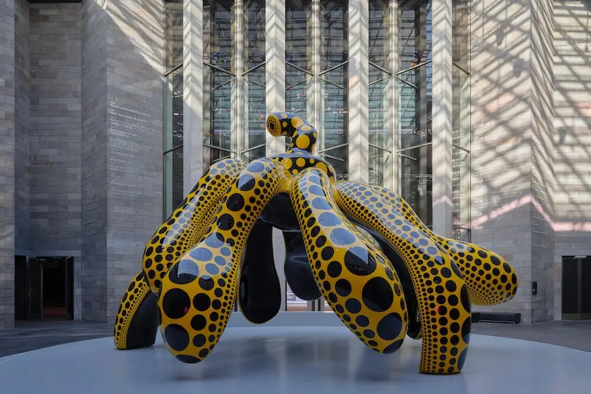 Large orange sculpture with tentacle-like structures supporting it. It has black polka dots covering it.