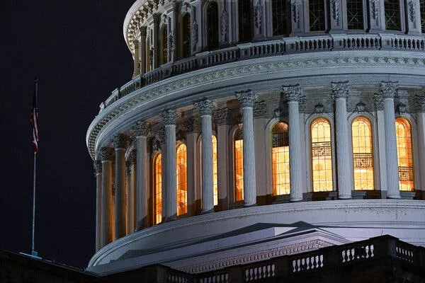 Part of the U.S. Capitol building's domed roof. Light shines from inside stained-glass windows between white pillars.