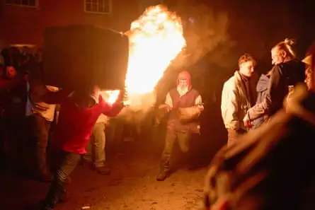 People hoist flaming barrels on their shoulders