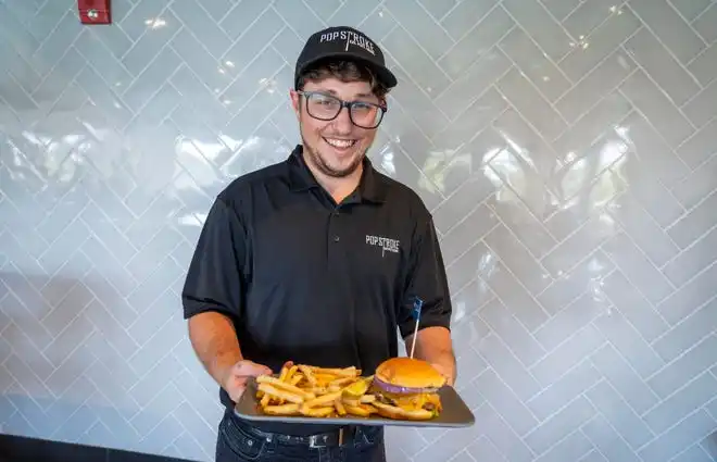 A waiter serves up a cheeseburger and fries at PopStroke on December 20, 2024, in West Palm Beach, Florida. Tiger Woods, Greg Bartoliand TaylorMade Golf Company are the owners.