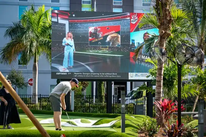 A patron putts next to a large screen broadcasting ESPN at PopStroke on December 20, 2024, in West Palm Beach, Florida. Tiger Woods, Greg Bartoliand TaylorMade Golf Company are the owners.