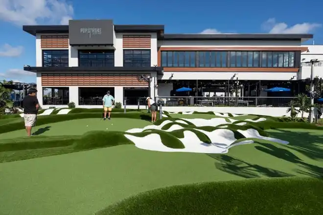 Daisy Leiva, right, Perry Sigouin and John Mall, left, play golf at PopStroke on December 20, 2024, in West Palm Beach, Florida. Tiger Woods, Greg Bartoliand TaylorMade Golf Company are the owners.